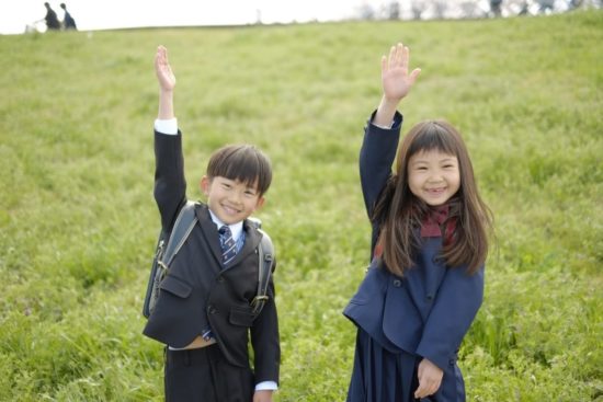 手を挙げる小学生の女の子と男の子の写真