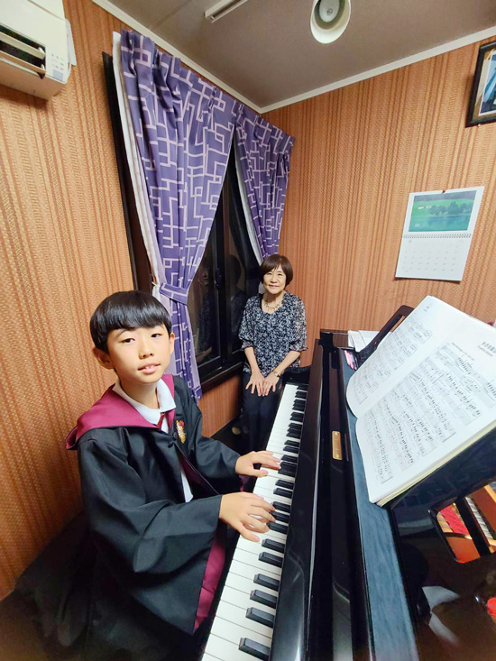 ピアノの前に座る生徒さんと先生の写真